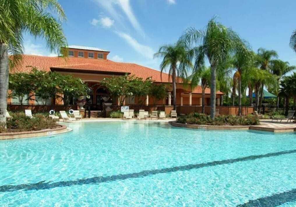 Une piscine entourée de chaises longues et de palmiers, le tout bordé par un bâtiment au toit rouge.