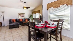 A dining area with a table set for four, a ceiling fan, and a living room with a sofa and a plant.