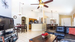 A spacious living room with a flat-screen TV, a leather sofa, a coffee table, and a ceiling fan.
