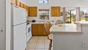 Una cocina compacta con armarios de madera, un refrigerador blanco, una estufa y una ventana con vista a follaje.