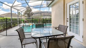 Un patio cubierto al aire libre con una mesa y sillas de vidrio, una piscina y vistas del paisaje circundante.