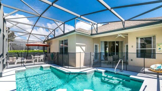 Un área de piscina con cerramiento de vidrio, mobiliario exterior y un porche cubierto.