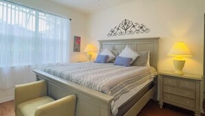 Un dormitorio con cama, dos mesitas de noche con lámparas, una silla y un elemento decorativo en la pared.