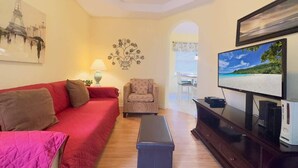 Una sala de estar con un sofá rojo, un sillón estampado, un televisor y una mesita.