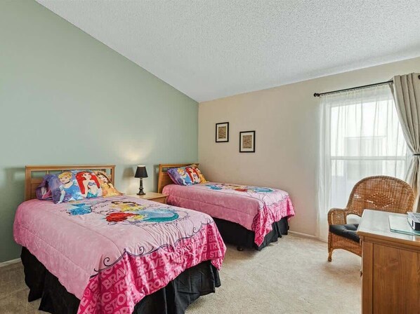 A bedroom with two beds, a chair, a desk, and a window with curtains.