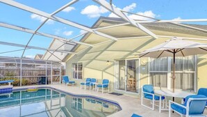 Ein Poolbereich im Innenbereich mit Glasveranda, blauen Liegestühlen und einem Tisch mit Sonnenschirm.