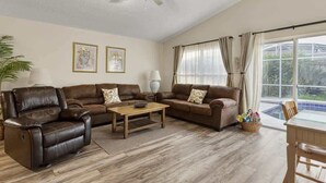 Ein geräumiges Wohnzimmer mit Ledersofas, einem Holztisch und einem Deckenventilator.