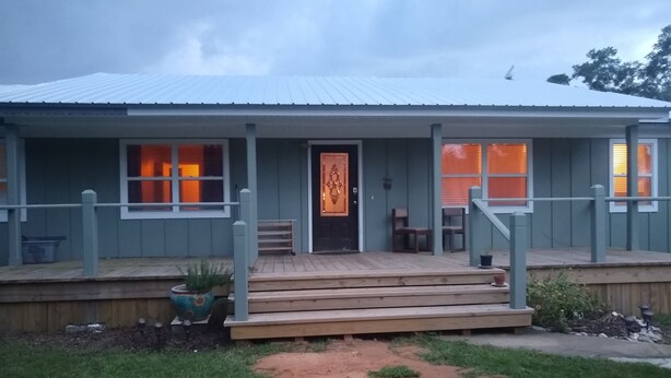 Ein zweistöckiges Haus mit Veranda, einer Haustür mit dekorativem Glasfenster und einem kleinen Garten mit einer Holzterrasse.