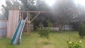 Ein Garten mit einer Holzrutsche, einem kleinen Baum und einer Rasenfläche.