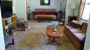 Ein Wohnzimmer mit einer Couch, einem Couchtisch, einem Fernseher auf einem Standfuß und einem Bücherregal.