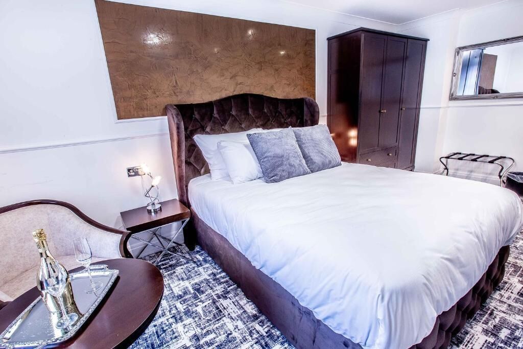 A hotel room with a large bed, a wooden headboard, a dark wardrobe, and a small table with a tray.