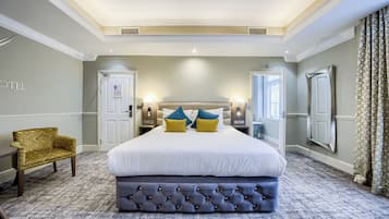 Quarto de hotel com uma cama grande, um banquinho estofado, um sofá e um espelho.