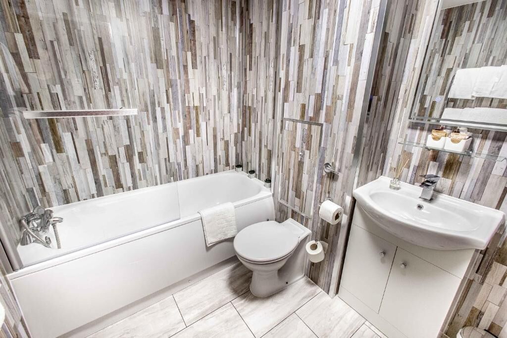 Une salle de bain équipée d’une baignoire, de toilettes et d’un lavabo, avec un mur au revêtement imitant le bois.