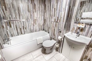 A bathroom with a bathtub, toilet, and sink, featuring a wood-textured wall. - The Grosvenor Hotel (Stratford-upon-Avon)
