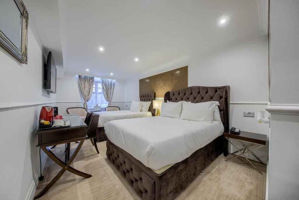 A hotel room with a large bed, a desk, a chair, a TV, and a window with curtains.