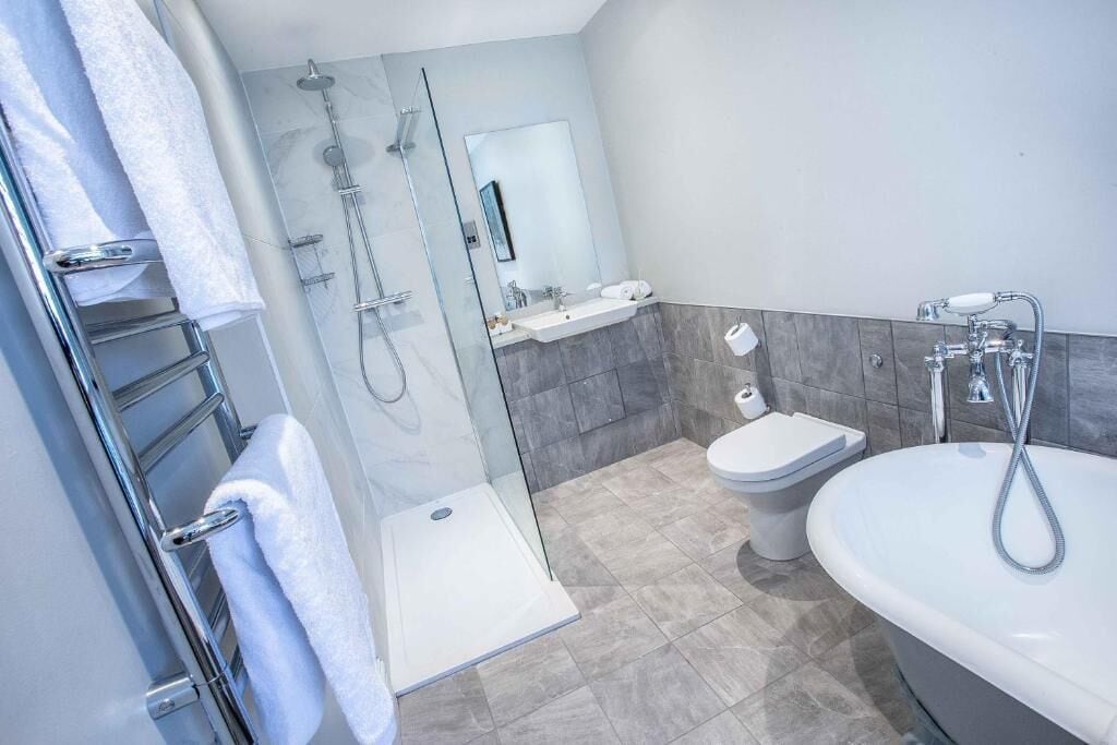 A modern bathroom with a glass-enclosed shower, a white sink, a toilet, and a freestanding bathtub.