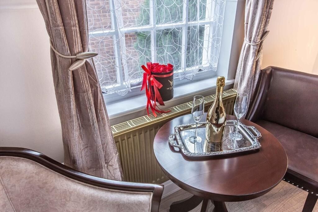 A cozy corner with a table set for two, a bottle of champagne, a glass, and a gift box on the windowsill.