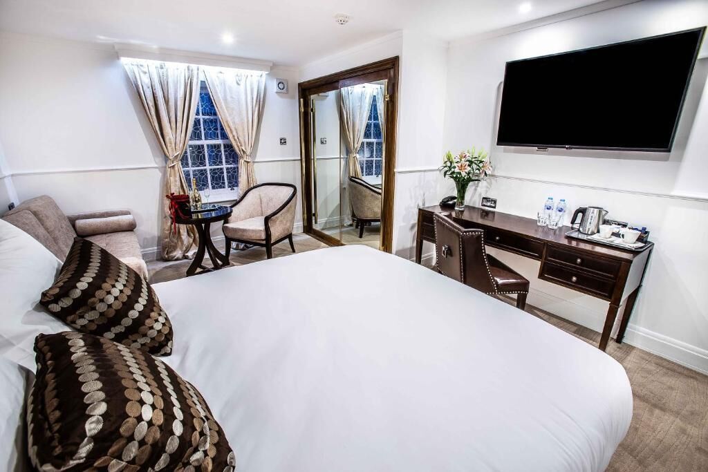 A hotel room with a large bed, a desk, a chair, a TV, and a window with curtains.