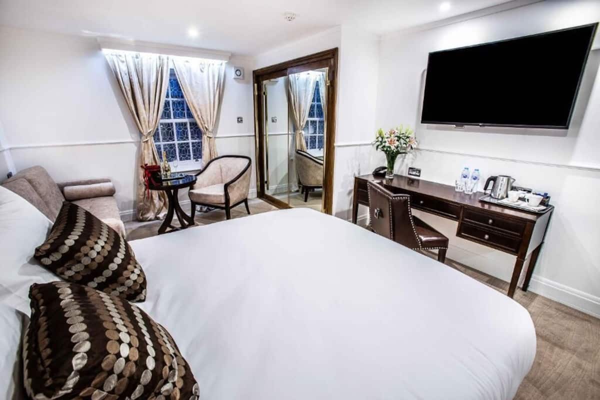 A hotel room with a large bed, a desk, a chair, a TV, and a window with curtains.