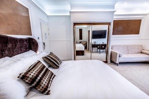Quarto de hotel com uma cama grande, um sofá, uma escrivaninha e um espelho.
