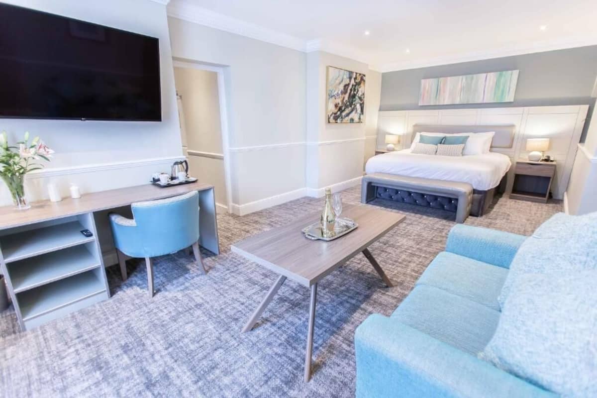 A modern hotel room with a flat-screen TV, a bed with white bedding, a sofa, a coffee table, and a desk with a chair.