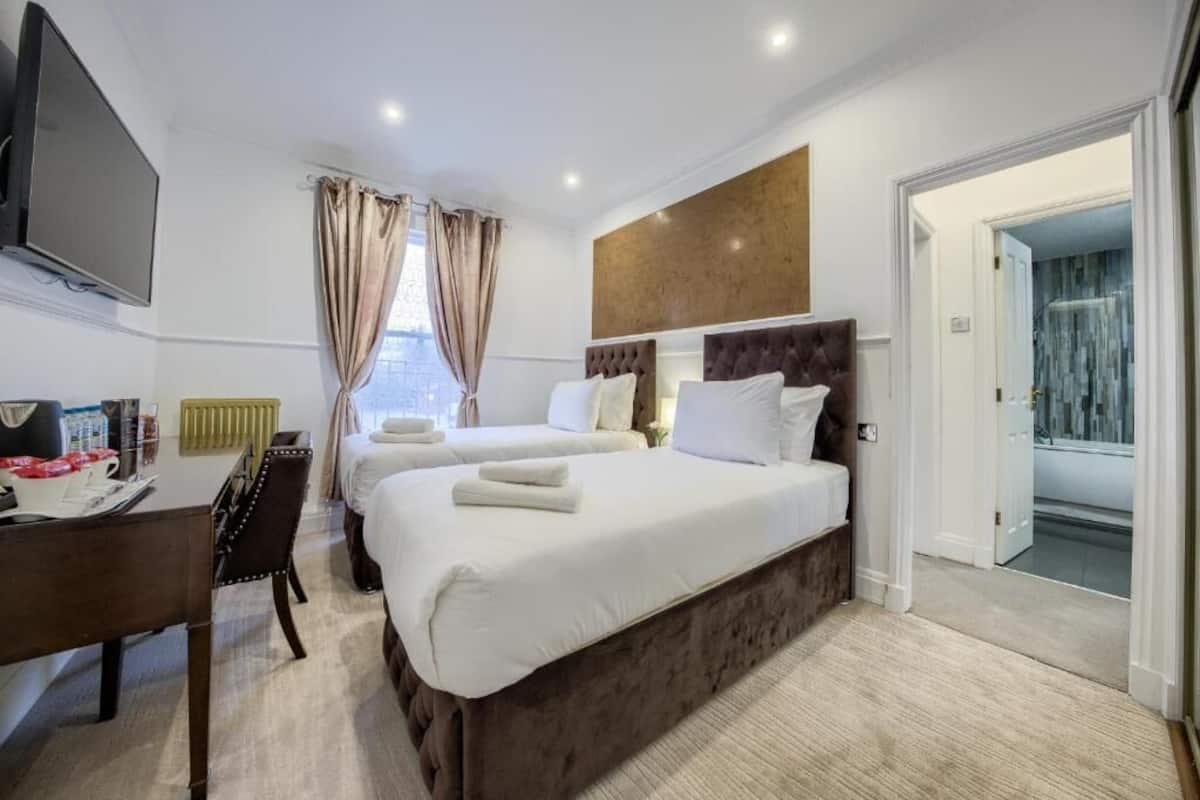 A hotel room with two beds, a desk, a flat-screen TV, and a view of the city.
