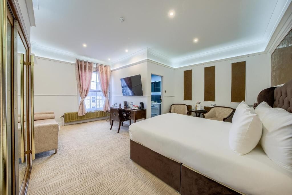 A hotel room with a large bed, a desk, a chair, a TV, and a window with curtains.