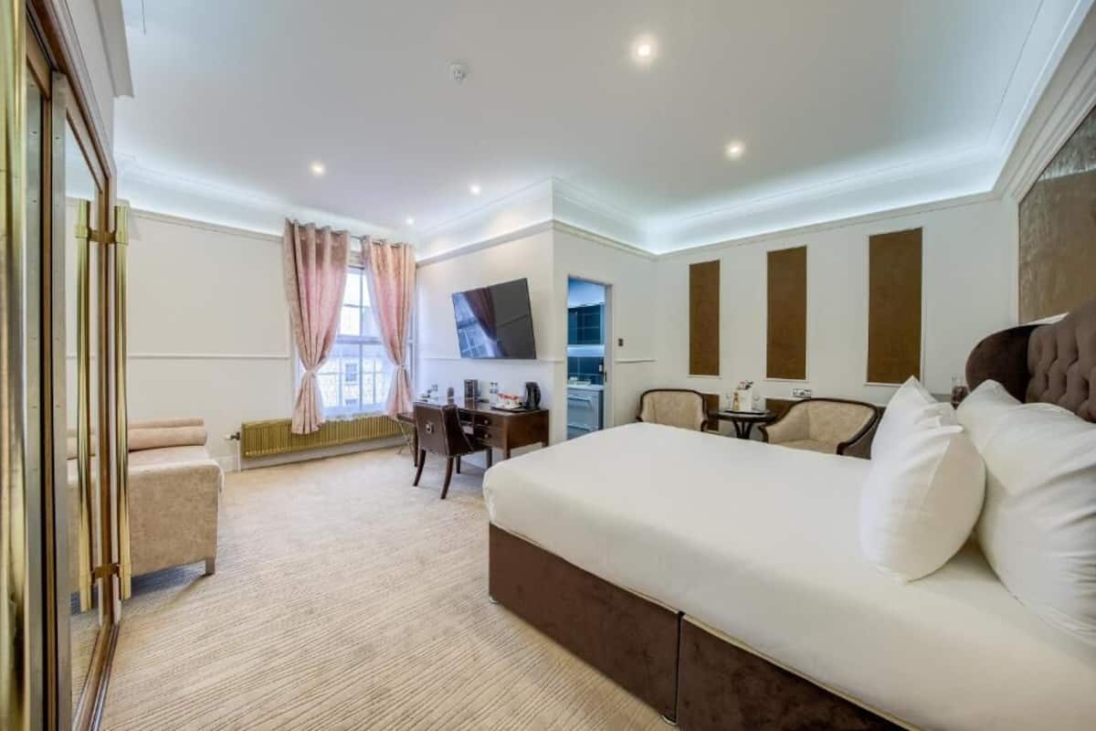 A hotel room with a large bed, a desk, a chair, a TV, and a window with curtains.