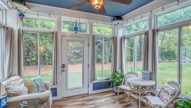 A sunroom with large windows, a ceiling fan, wicker furniture, and a wooden floor.