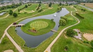 A golf course with a pond, a bridge, and a fountain.