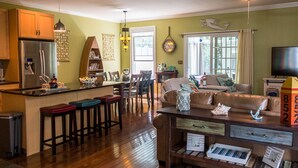 A spacious living area with a wooden floor, a kitchen with a refrigerator, and a dining area with chairs and a table.