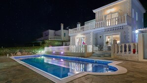Une grande maison moderne avec une piscine, de nuit.