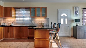Une cuisine avec des meubles en bois, un dosseret carrelé, un îlot central avec des tabourets et une porte surmontée d’une arche décorative.
