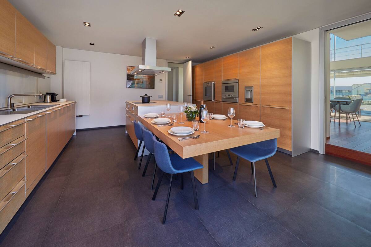 Una cocina moderna con una mesa de madera para cuatro comensales, sillas azules y electrodomésticos de acero inoxidable.
