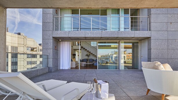 A rooftop terrace with lounge chairs, a table with champagne, and a view of a modern building with a glass entrance. - Hyatt Regency Madrid Residences (Madrid)