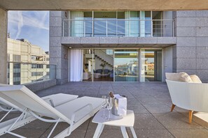 Terraza en la azotea con sillones, una mesa con champán y vistas a un edificio moderno con entrada de cristal.