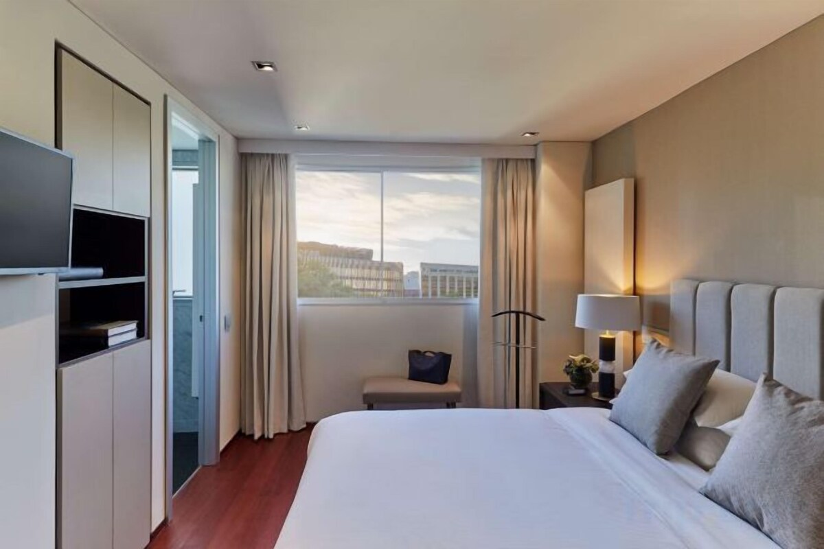 A hotel room with a bed, a television, a desk, and a window with curtains.