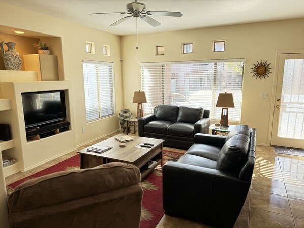 A living room with a TV, two sofas, a coffee table, and a ceiling fan. - Relax in this Beautiful Oro Valley Condo - Right Next to the Pool! (Oro Valley)