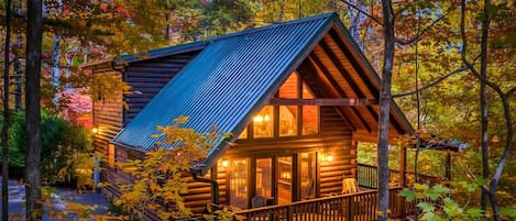 A log cabin with a metal roof, wooden deck, and a stone foundation.