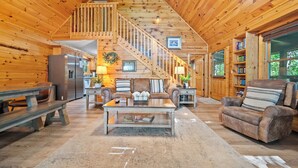 A spacious living room with a wooden interior, a staircase, a sofa, a coffee table, and a bookshelf. - ★Gray Fox Den★ • Secluded 3BR • Theater, Hot Tub, Arcade • Near Smokys/Downtown (Gatlinburg)