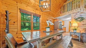 A wooden cabin interior with a dining table, chairs, a refrigerator, and a staircase. - ★Gray Fox Den★ • Secluded 3BR • Theater, Hot Tub, Arcade • Near Smokys/Downtown (Gatlinburg)