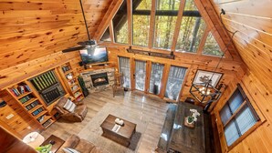 A cozy cabin interior with a fireplace, wooden walls, and large windows offering a forest view. - ★Gray Fox Den★ • Secluded 3BR • Theater, Hot Tub, Arcade • Near Smokys/Downtown (Gatlinburg)
