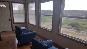 A room with two blue armchairs, a wooden floor, and large windows offering a view of a rural landscape. - Room with a View (Monticello)