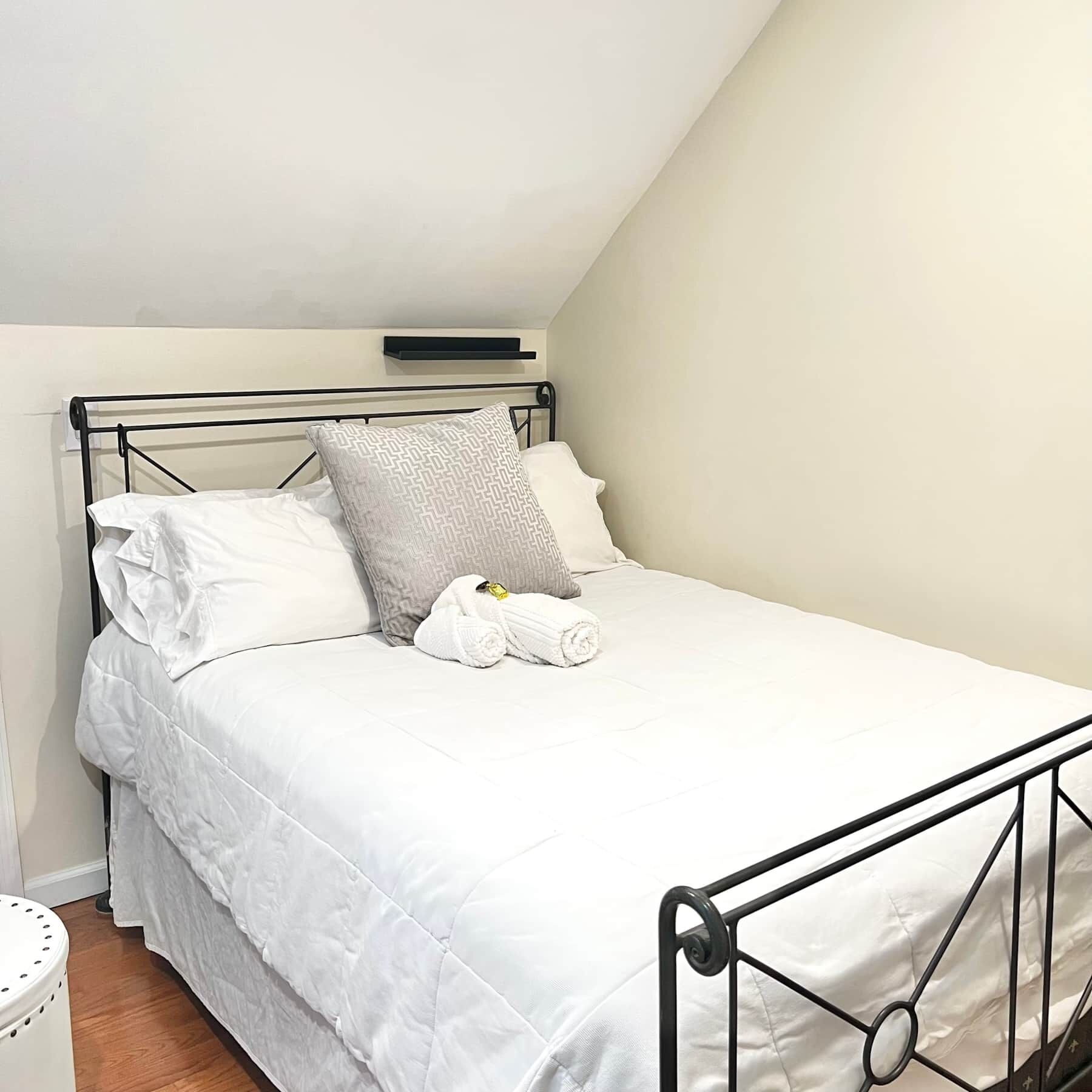 Een net opgemaakt bed met wit beddengoed en twee kussens, een klein nachtkastje en een wandplank boven het bed.
