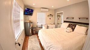 A bedroom with a bed, a TV, a refrigerator, a desk, and a window with blinds. - Private 3Br Apt: King-2Queen -PetPally -LTR-STR (Bay Shore)