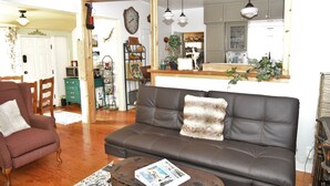 A living room with a brown leather sofa, a patterned armchair, and a coffee table with a magazine. A large mirror spans the wall above the sofa, reflecting the room. - ❤Riverfront Paradise - Butterfly Ranch on the River❤ (Dunsmuir)