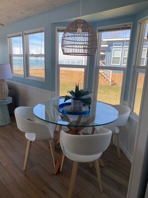 A dining area with a glass table, white chairs, and a hanging light fixture.