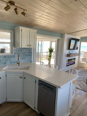 A kitchen with a large island, white cabinets, a dishwasher, and a view of the ocean through large windows.