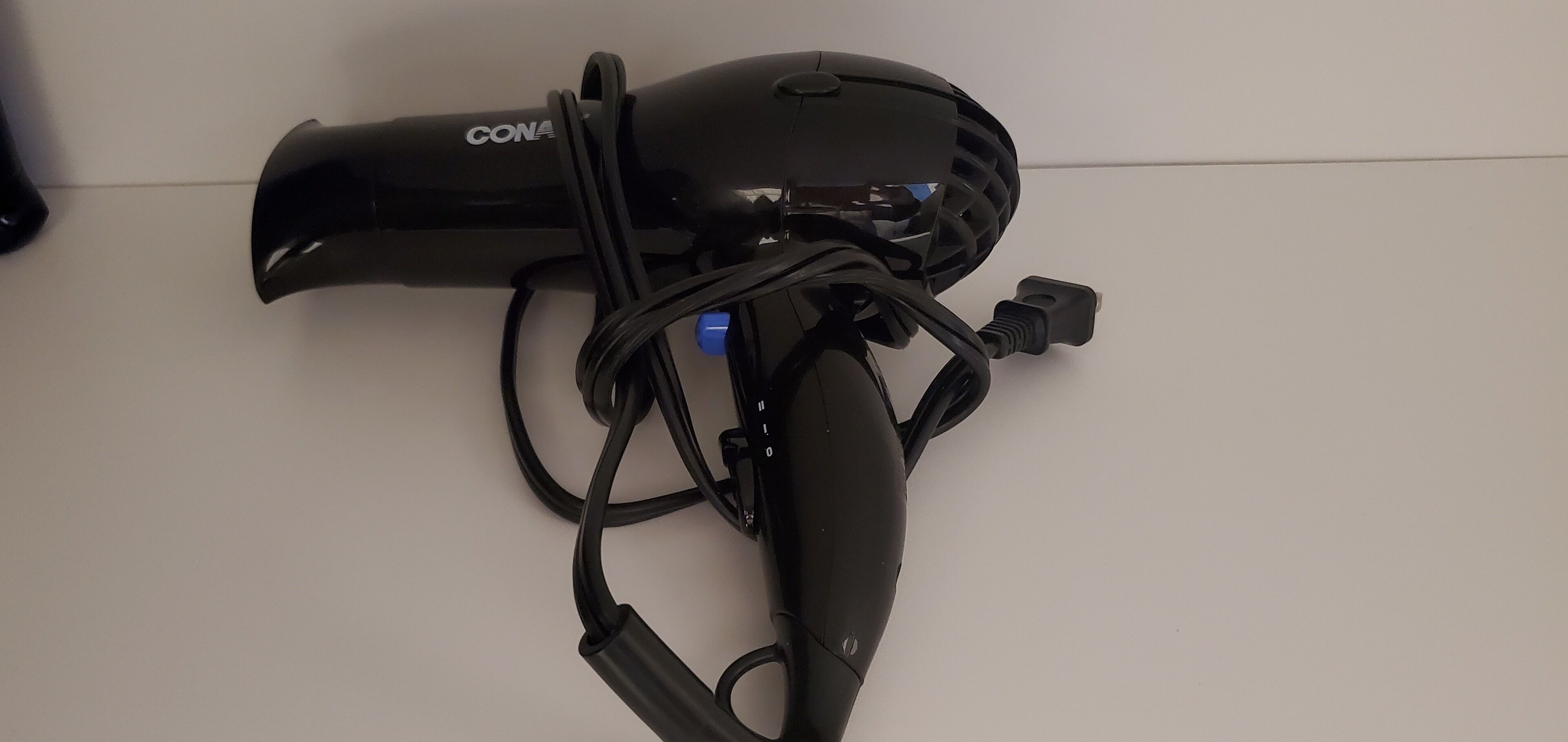 Un secador de pelo negro con cable y un enchufe sobre una superficie blanca.
