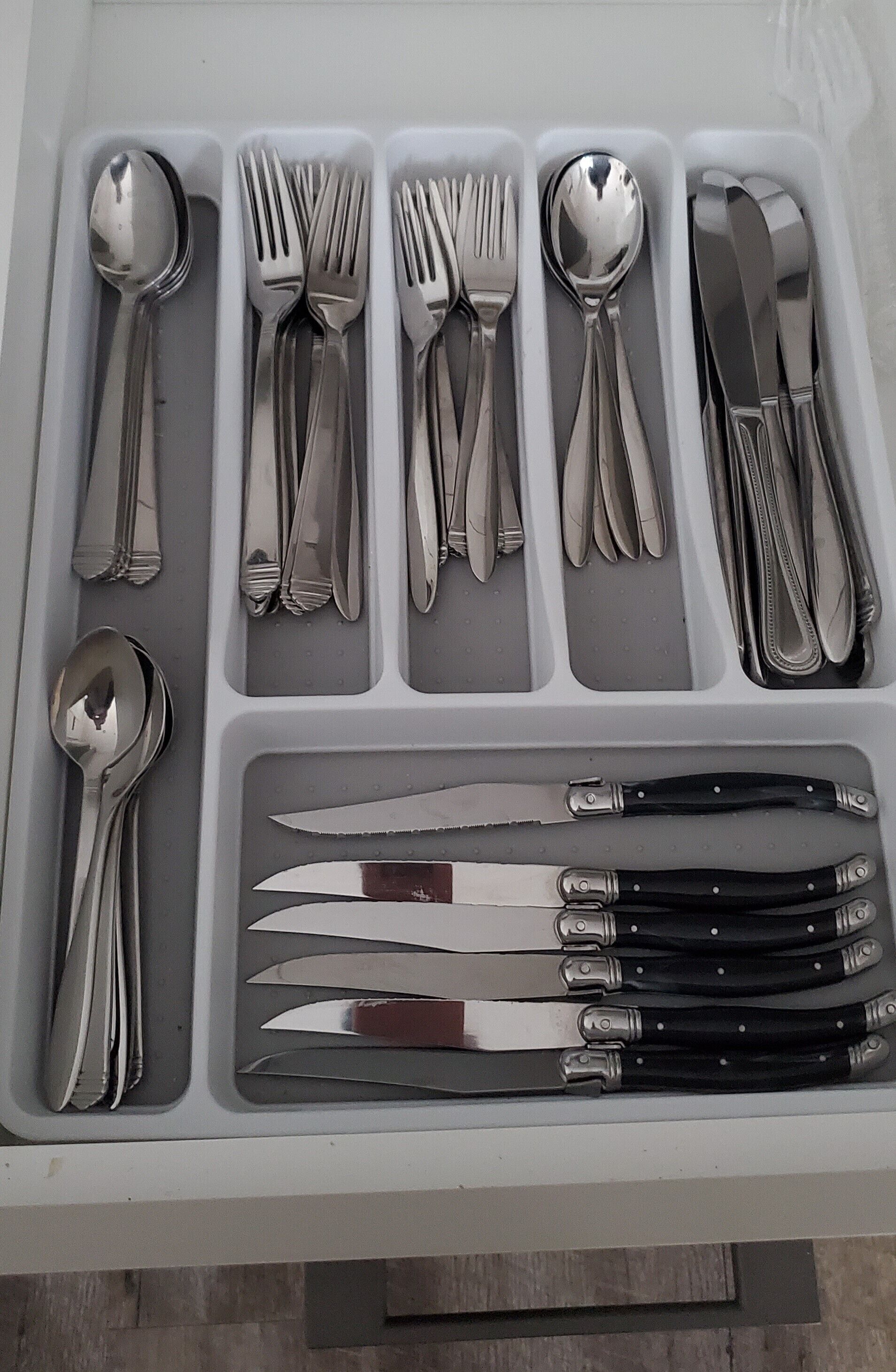 Uma gaveta com diversos utensílios, incluindo colheres, garfos, facas e um conjunto de facas de carne.